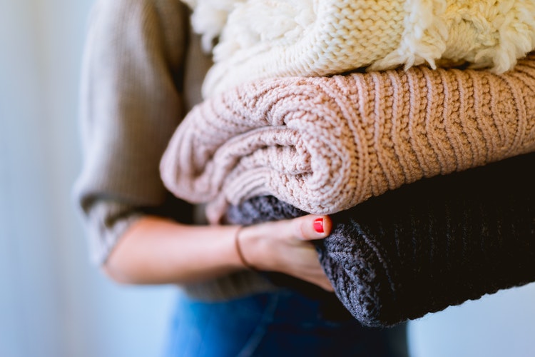 jesenske foto ideje za instagram - dekle z zloženimi puloverji v rokah